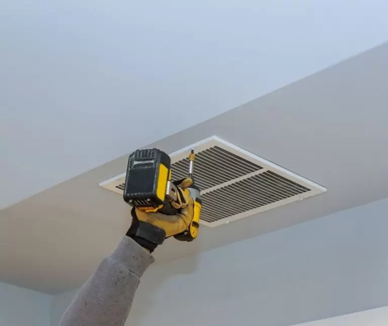 HVAC Technician using a drill to unscrew an HVAC vent